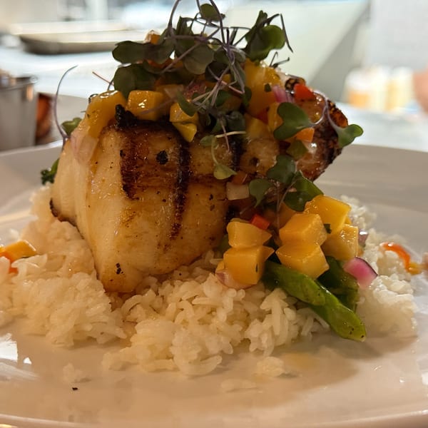 Grilled fish with mango salsa and microgreens, served over white rice on a white plate.