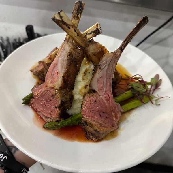Plated lamb chops with mashed potatoes, asparagus, and a red wine reduction.