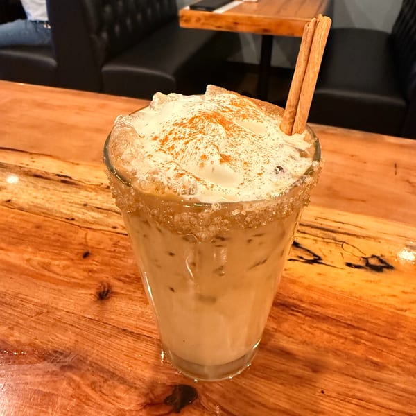 Iced coffee with whipped cream, cinnamon, and a sugar-rimmed glass on a wooden table.