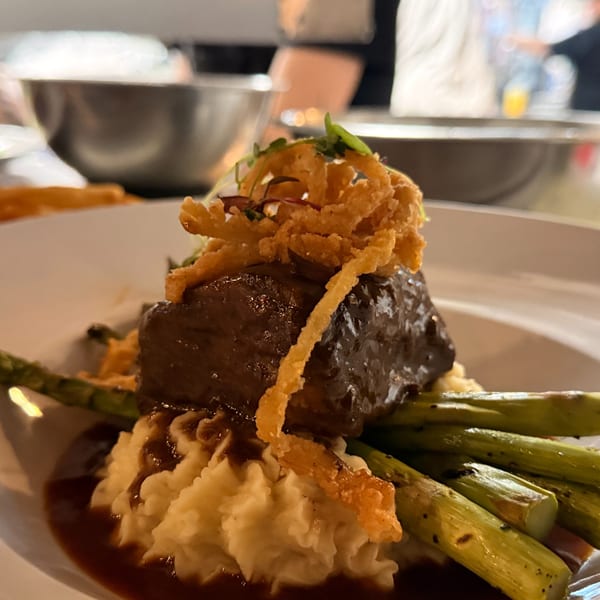 Braised short rib with mashed potatoes, asparagus, gravy, and crispy fried onions on a white plate.