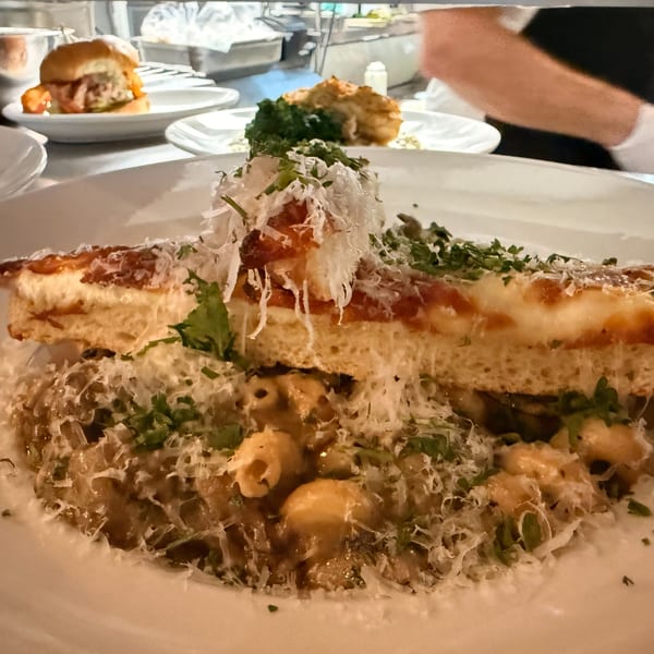 A Live Fire Chefs dish with mac and cheese topped with a slice of pizza and grated cheese.