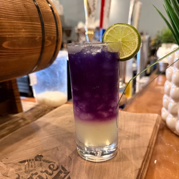 A vibrant purple and white layered cocktail with ice and a lime slice on a wooden bar.