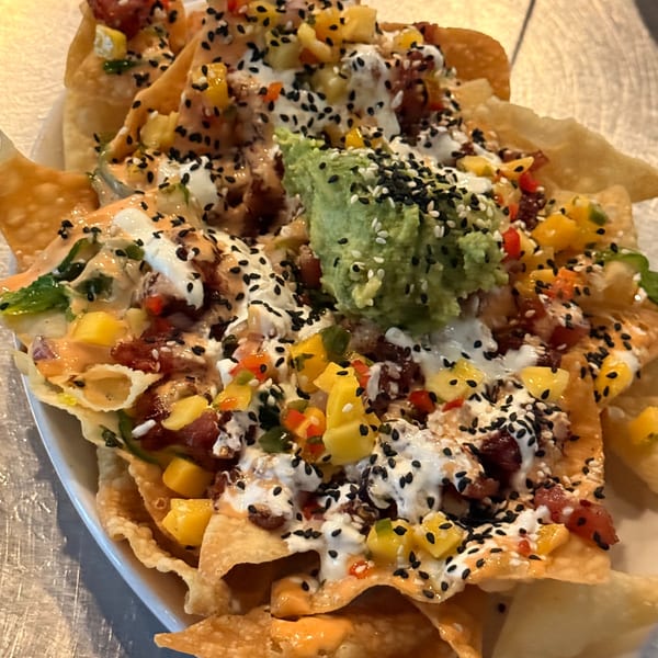 Close-up of Live Fire Chefs' Italian-American fusion nachos with guacamole, mango, and sesame seeds.