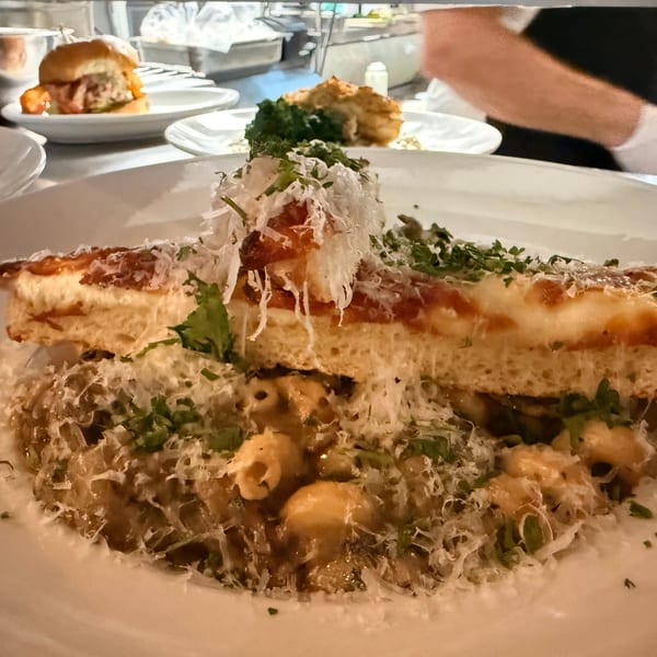 A close-up of mac and cheese topped with a slice of cheesy bread and fresh herbs.