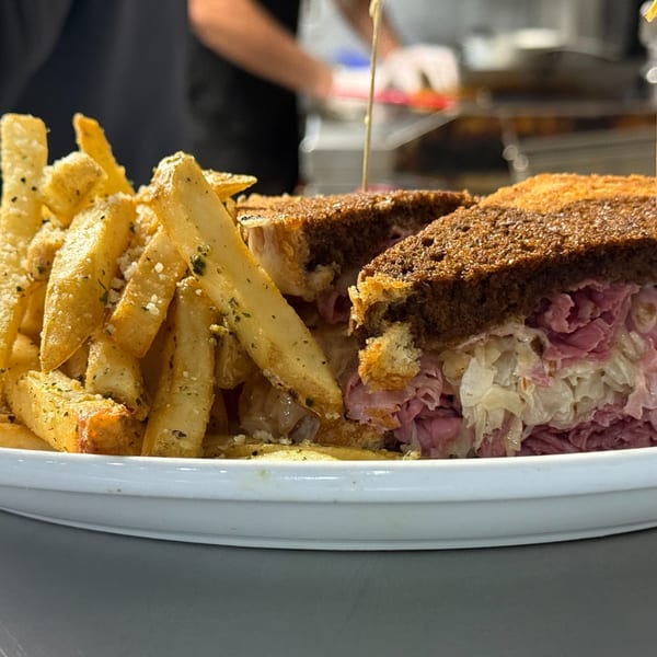 A reuben sandwich with corned beef and sauerkraut, served with a side of seasoned french fries.