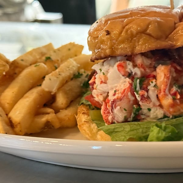 A Live Fire Chefs lobster roll with lettuce and tomato, served with a side of french fries.