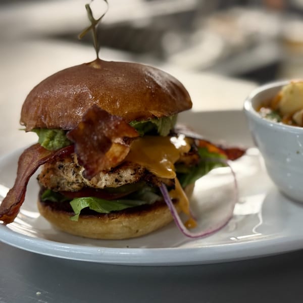 A Live Fire Chefs burger with bacon, avocado, and red onion, served with a side dish.