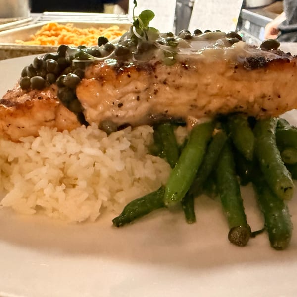 Grilled salmon with capers, white rice, and green beans on a white plate.